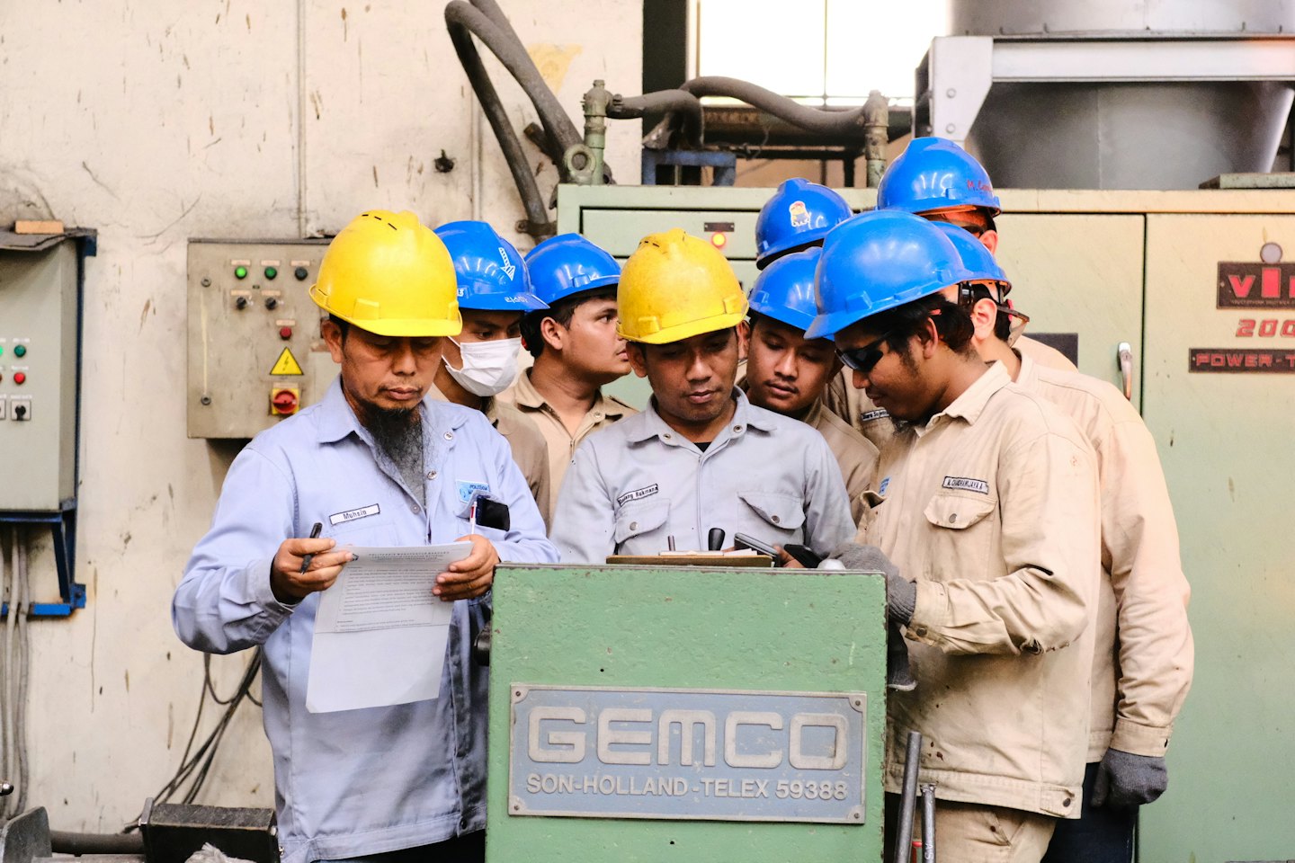 Male factory workers in hard hats inspect machinery.